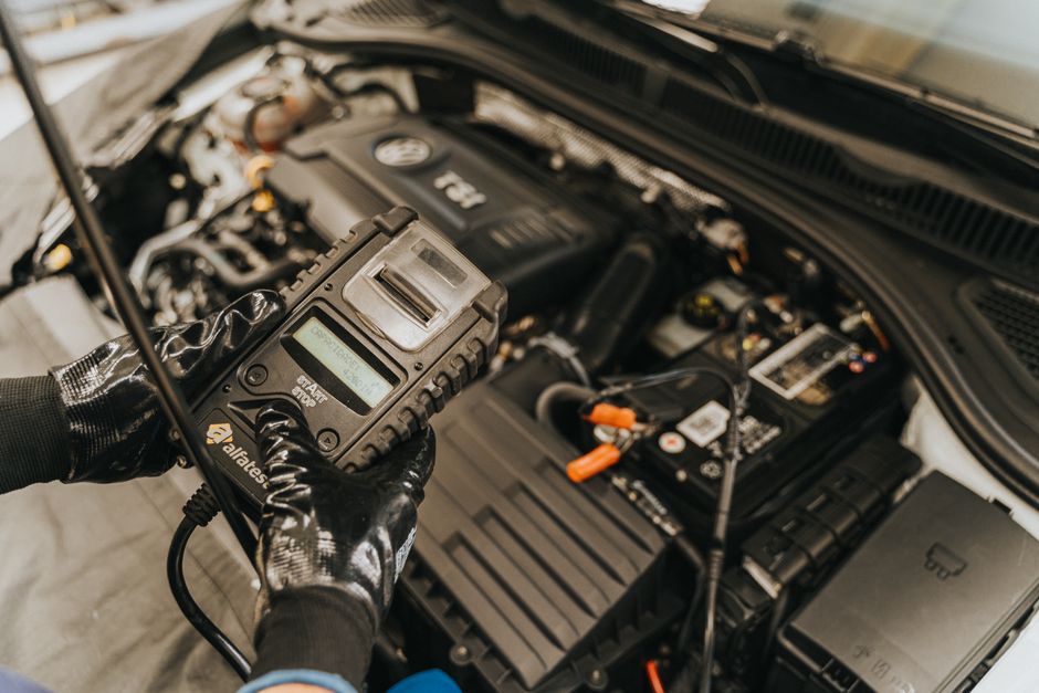 Multimètre branché en série sur la cosse négative d'une batterie de voiture dans un garage